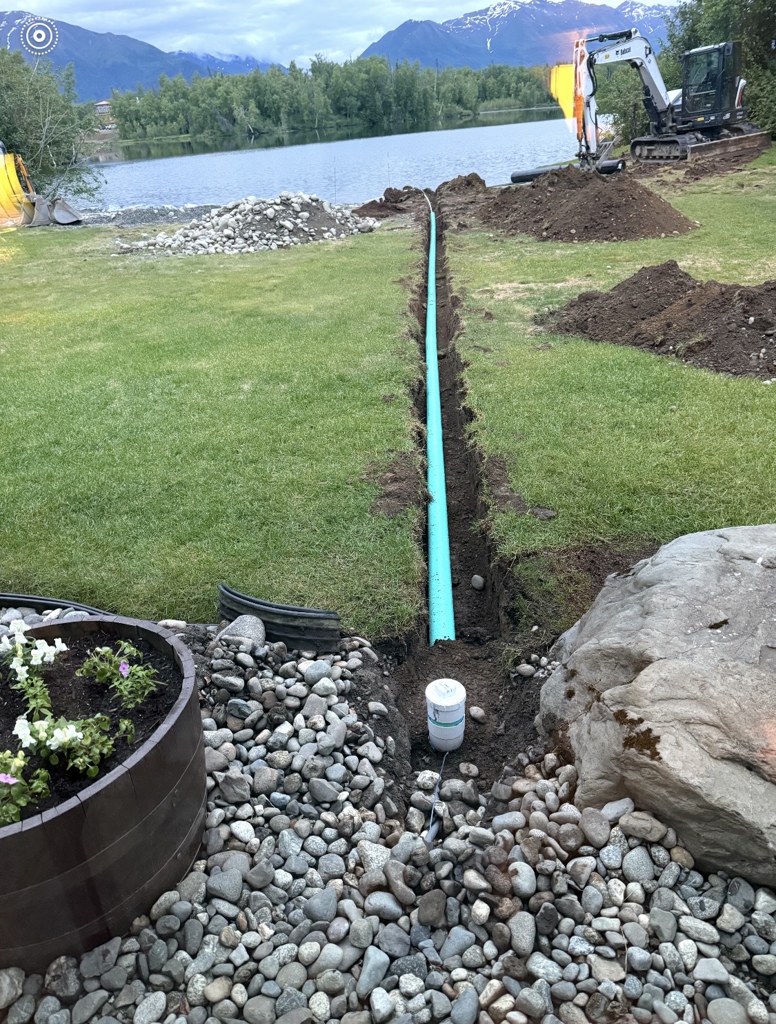 Septic system trench with green PVC pipe running across a residential lawn, lake and mountains in background