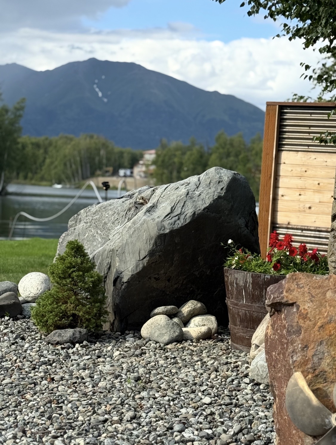 Finished landscaping with large boulder feature, river rock, and flower planter with Alaska mountains in background