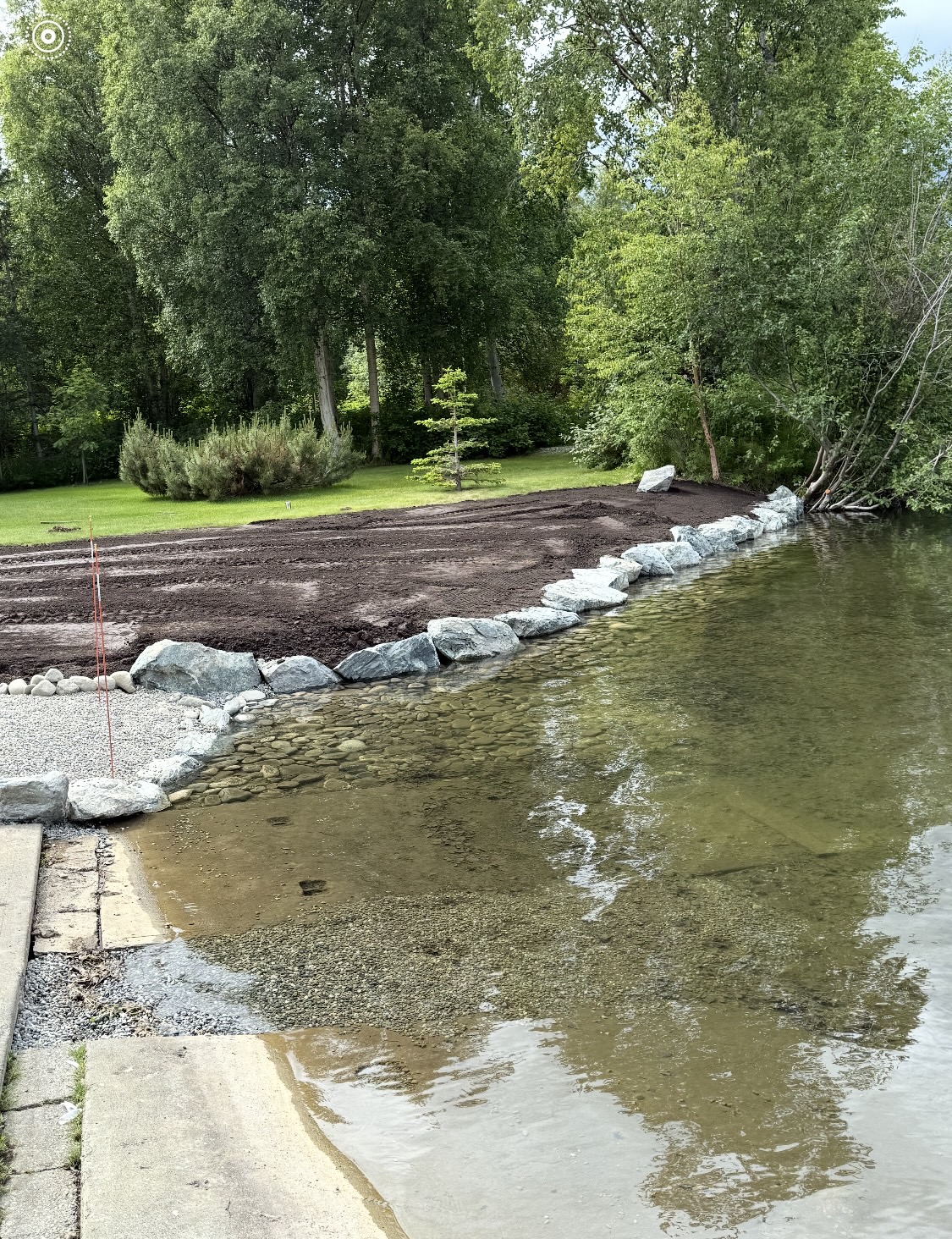 Completed riprap rock wall and graded topsoil along a residential lakeshore