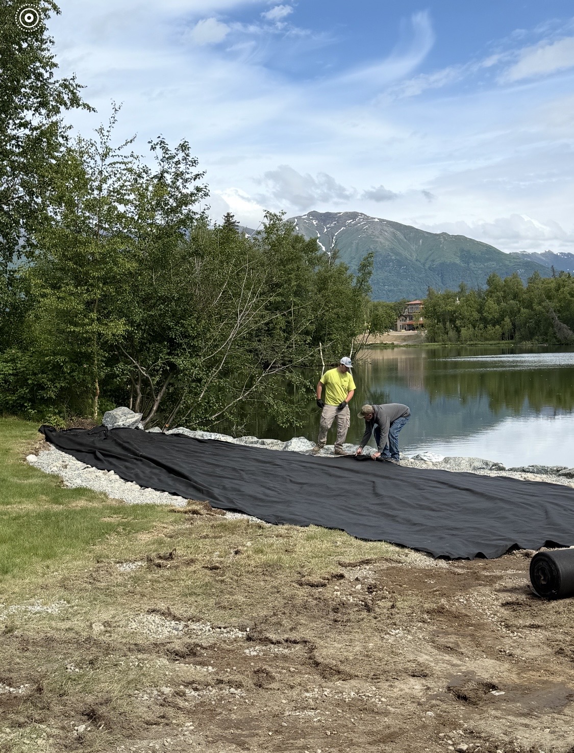 Workers laying geotextile fabric over a riprap shoreline stabilization — Mat-Su Valley, Alaska