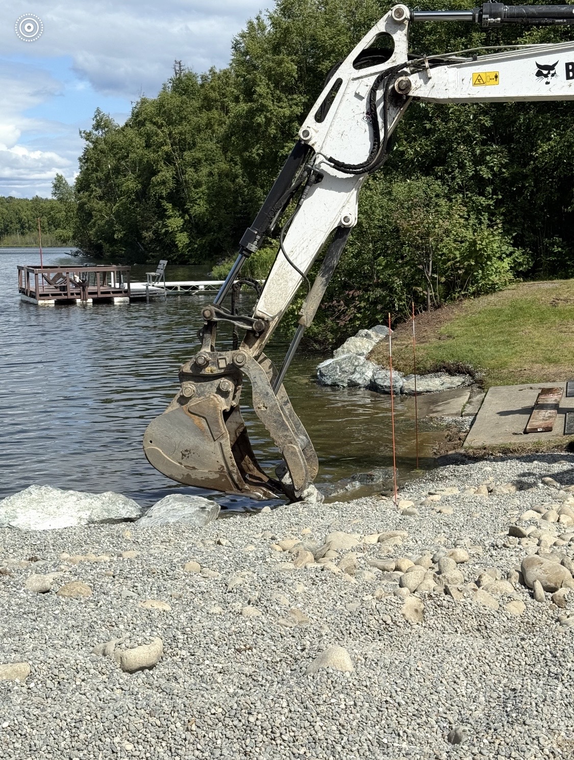 Bobcat excavator bucket working at the waterline placing riprap rocks for shoreline stabilization