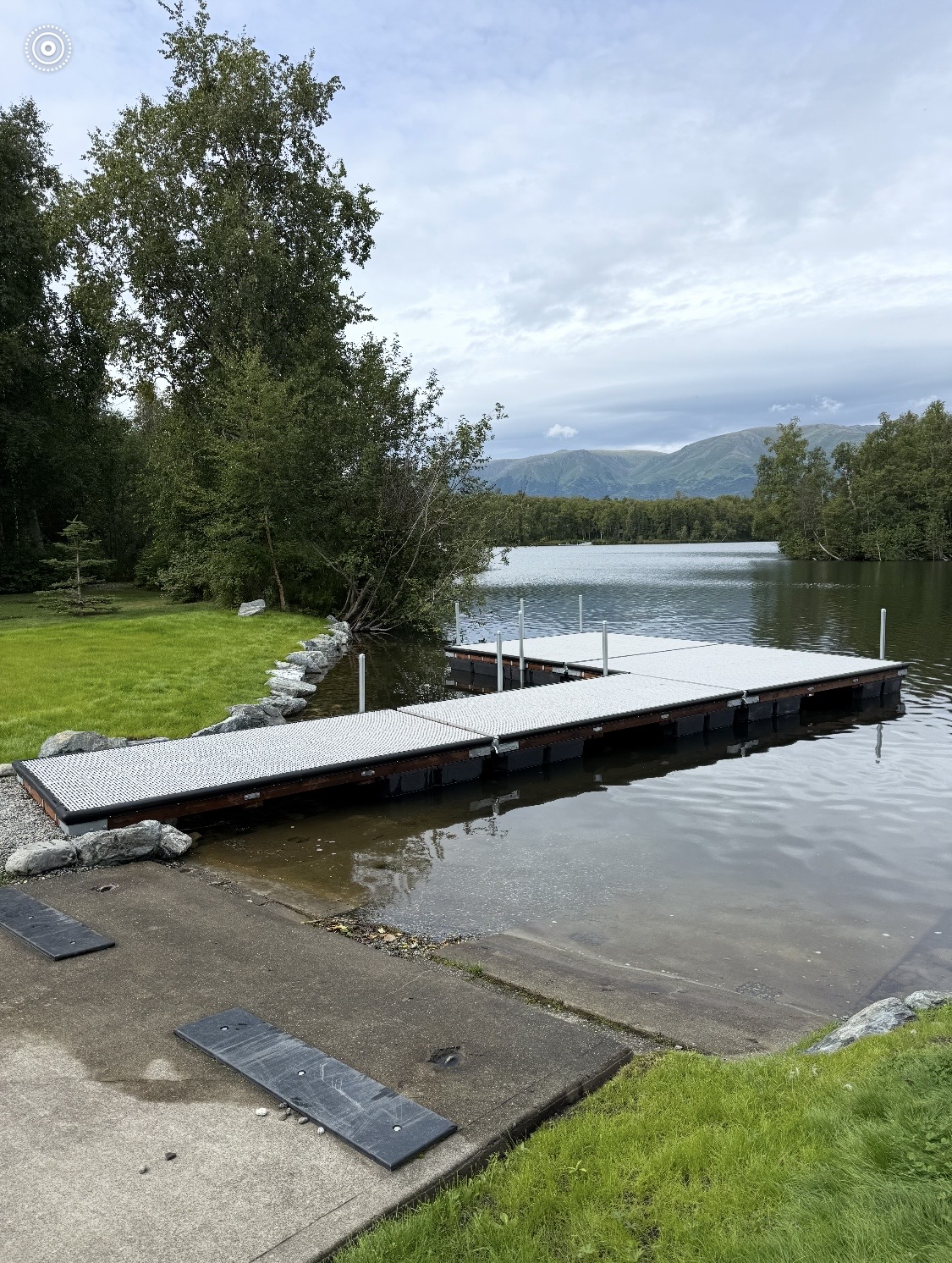 Completed dock, concrete approach, riprap shoreline, and manicured lawn — a finished residential project in the Mat-Su Valley